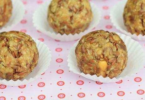 Peanut Butter balls displayed in white paper cups on a pink tablecloth.