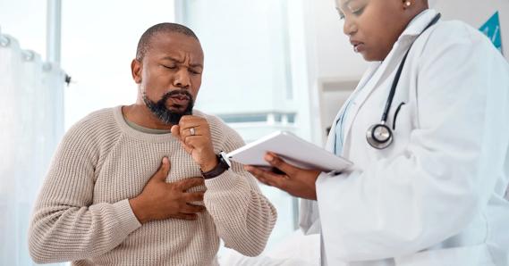 Patient coughing, with hand on chest, as healthcare provider checks chart