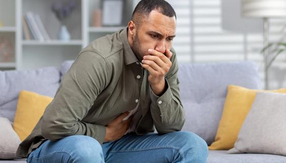 Man sitting on couch with hand over mouth and other hand holding stomach