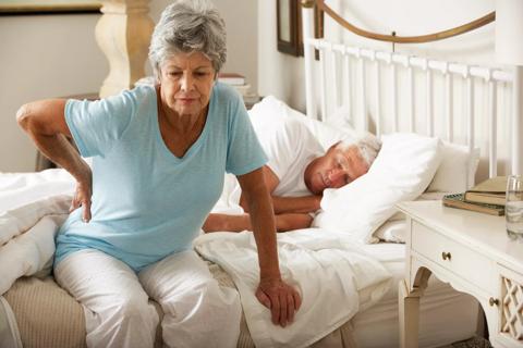 A senior woman suffering from a backache getting out of bed.