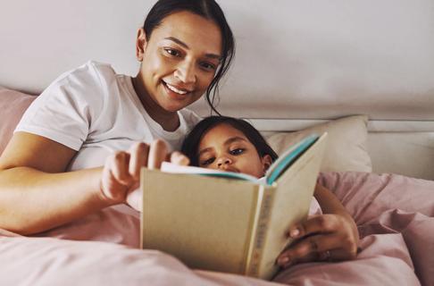 Smiling caregiver reading to child in bed