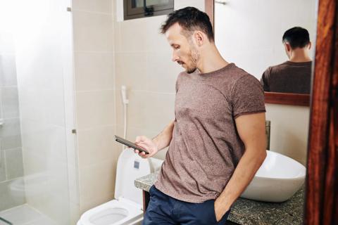 Man leaning against sink in the bathroom on their phone