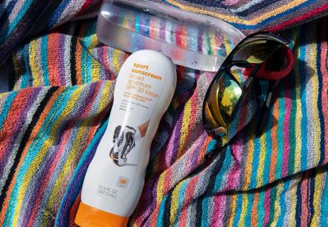 sunscreen water and sunglasses on beach blanket