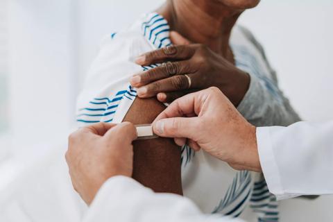 Healthcare provider placing bandaid on upper arm after a shot