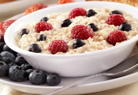 A white bowl filled with hot oatmeal and fresh raspberries and blueberries on a white plate.