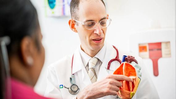 physician pointing to a heart model and speaking to a woman
