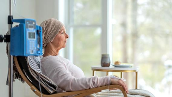 Person receiving cancer infusion therapy sitting in chair, head wrapped in scarf, gazing out window