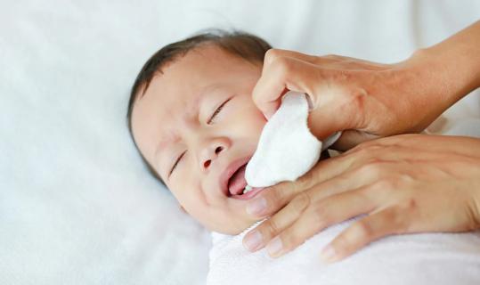 Hands wiping a baby's mouth area with a washcloth