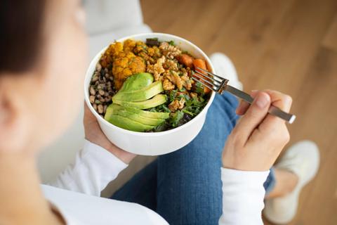 Person holding bowl of healthy grains, beans, avocado and other vegetables