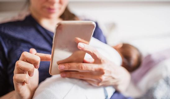 Mother using phone while holding newborn