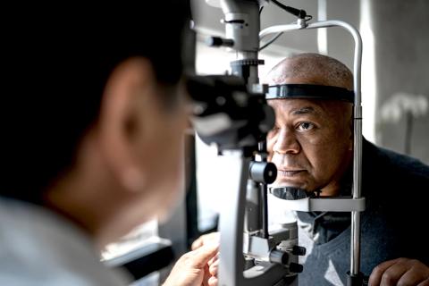 Person with head against eye exam equipment, with provider looking through other end at eyes