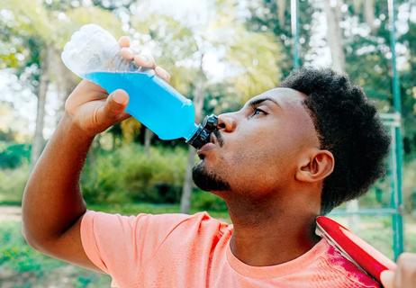 Person drinking sports drink with electrollytes while taking a break from tennis.