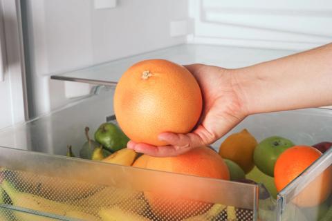 Hand taking a grapefruit out of the fruit drawer in a fridge