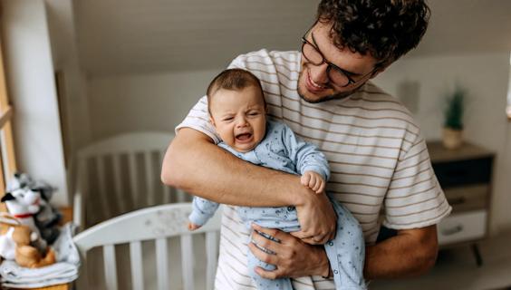 Smiling caregiver holding crying baby in nursery, crib nearby