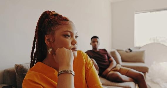 Person sitting defiantly with hand on chin, separate from other person on couch