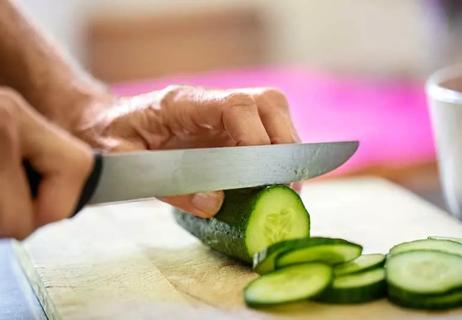 Person chopping a cucumber on cutting board.