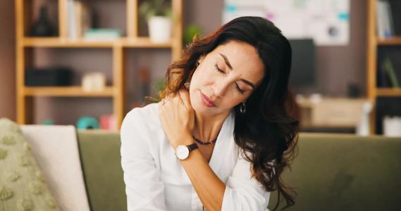 Woman sitting with eyes closed, rubbing her neck
