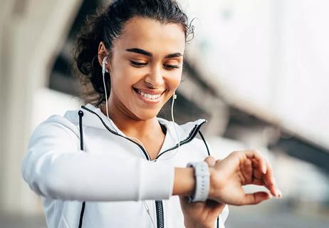 Individual wearing headphones and athletic clothing checks a fitness tracker
