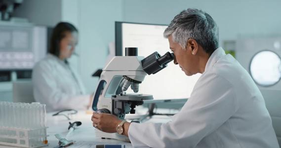 Scientists in white lab coats working in a lab, using microscope