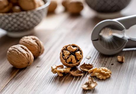 Shelled walnut cracked for eating in foreground with a bowl of walnuts in background.