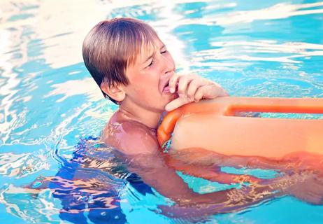 young person in swimming pool holding onto floatation device while coughing heavily.