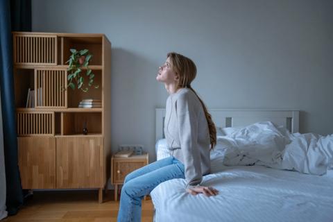 Person sitting on edge of bed, staring up at ceiling