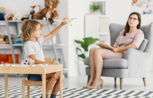 Child playing with toys, being assessed from afar by a healthcare provider
