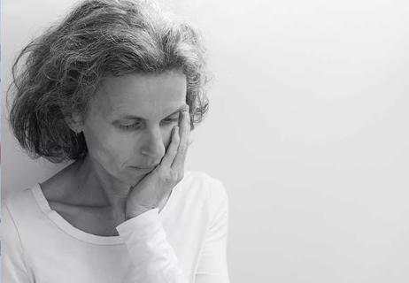 Elderly woman resting her hand on her face, appearing solemn and sad.