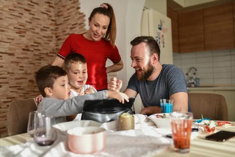 A family sitting at the kitchen table, with cups and plates around, playing on a tablet together