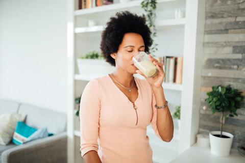 Person drinking a milky smoothie from glass in living room