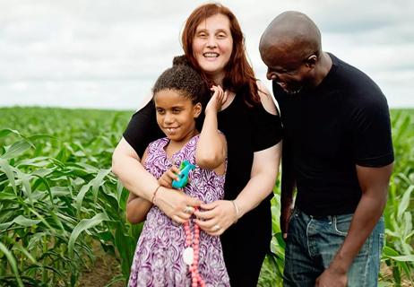 two adults and a child posing and smiling in a corn field