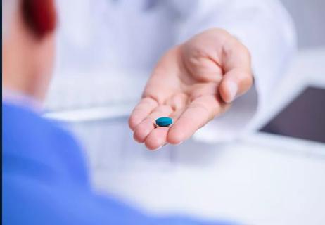 Physician's hand holding a blue pill in the palm of his hand, offering it to a patient.