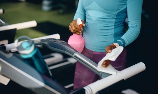 Person with spray bottle and wipe, cleaning gym equipment