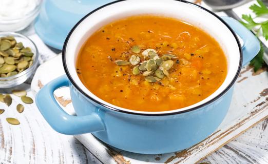 A light blue pot of lentil and pumpkin soup with pumpkin seeds and spices on top