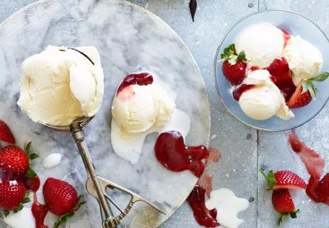 Scoops of vanilla ice cream on marbled plates with strawberries and syrup.