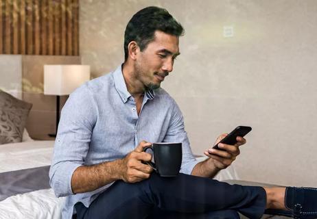 Man looking at smartphone while sitting on bed scheduling an appointment online.