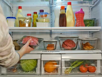 Person placing ground meat in their fridge, which is filled with fresh foods