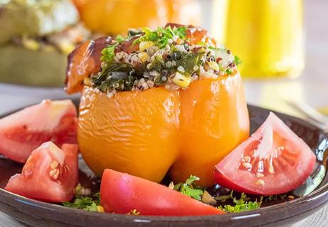 A yellow pepper stuffed with a veggies and quinoa mix, and surrounded by tomato wedges