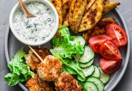 A plate with potatoes, cucumbers, lettuce, sliced tomatoes and some kind of white dipping sauce