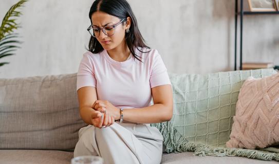 Person sitting on couch, scratching itchy skin on their arm, frowning