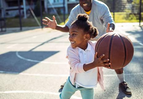 Kid playing basketball with parent.