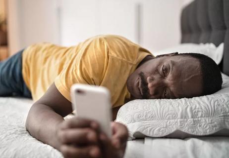 older man sick on bed with phone in hand