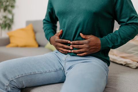 Person sitting down, holding abdomen with both hands