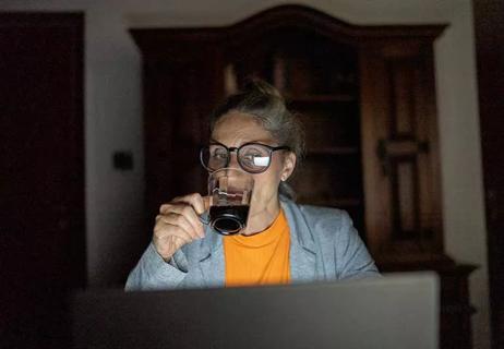 person drinking coffee at computer at night
