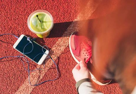 Smartphone and smoothie drink on ground next to a person lacing athletic shoes
