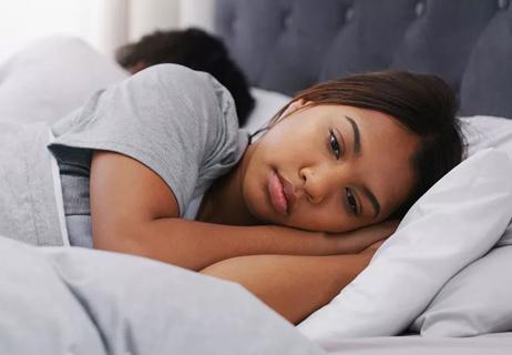 Sad woman laying awake in bed on her side, back to back with partner.