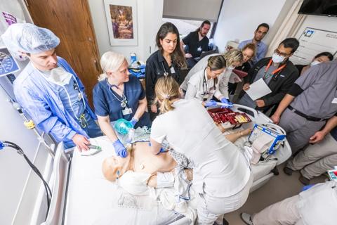 Medical team stands around manikin in hospital bed