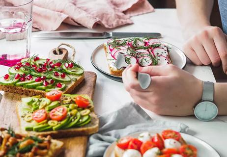 hand cutting into avocado toast with radish with other types of avocado toast on the table