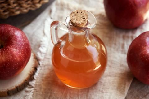 Glass cruet of apple cider vinegar with red apples around it on a table