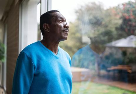 Older Black man gazes out the window with his reflection lightly reflected back at him